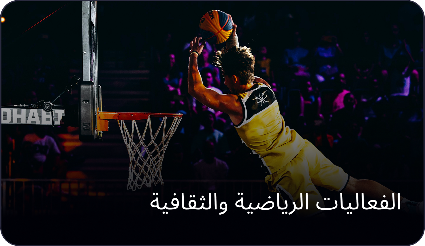 Professional basketball player performing a slam dunk in a brightly lit indoor sports arena in the Middle East